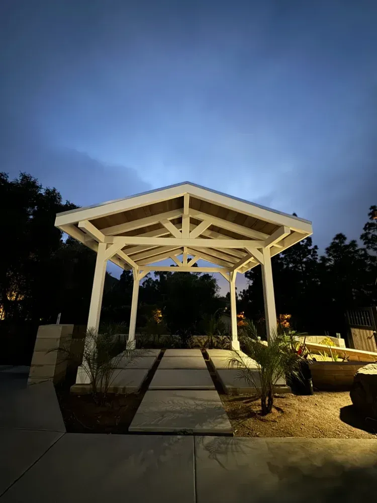 White gazebo at dusk with pathway, surrounded by trees and soft lighting.