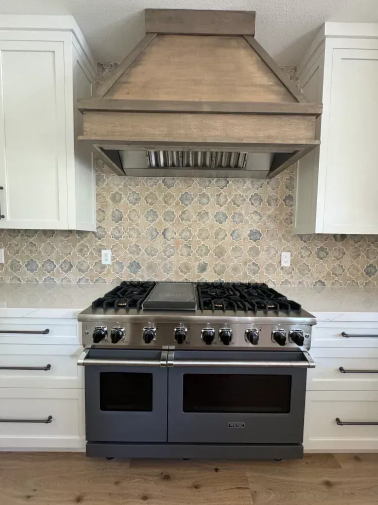 Kitchen with a large range stove, light-colored cabinets, a wooden range hood, and patterned backsplash.