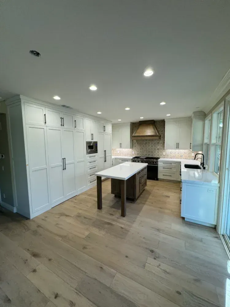 Newly renovated kitchen with white cabinets, a wooden island, and light wood floors. A black stove and copper range hood are in the background.