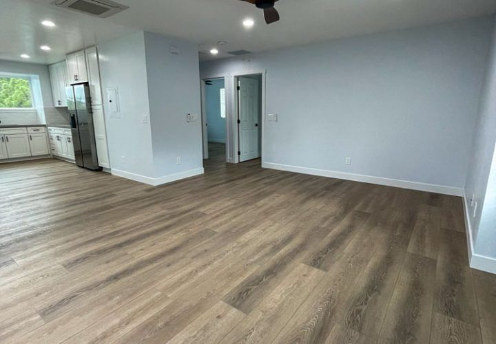 Empty apartment interior with light blue walls, wood-look flooring, and a view into a hallway.