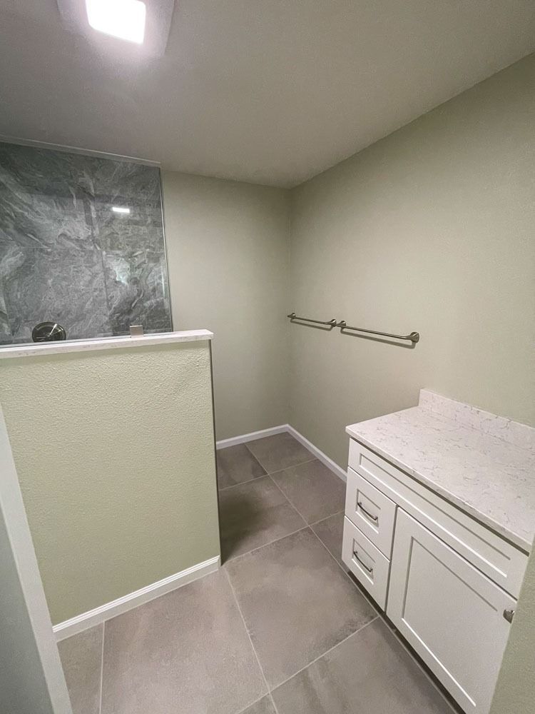 A bathroom with green walls and gray tile. A white vanity and shower with dark marbled stone are visible.