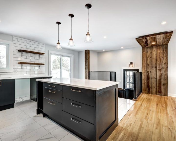 Modern kitchen with a black island, white countertops, wood accents, and hanging pendant lights.