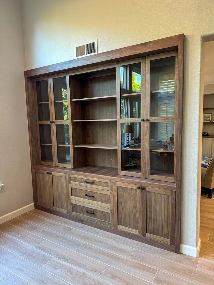 Custom-built wooden cabinet with glass-doored display shelves, solid cabinet doors, and drawers, set against a tan wall.
