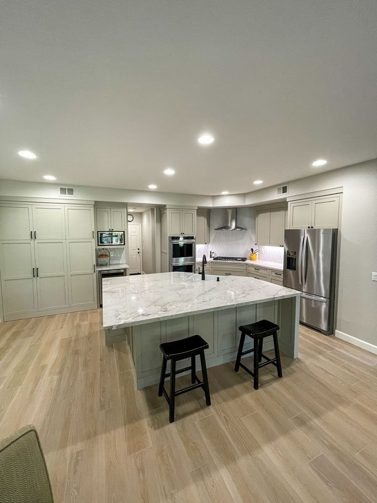 Spacious kitchen with a large island, light cabinets, granite countertop, and stainless steel appliances. Two black stools sit at the island.