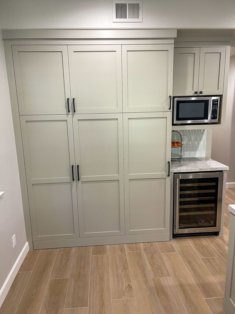 Built-in pantry and kitchen cabinets in light gray.  Includes a microwave, wine cooler, and marble countertop.