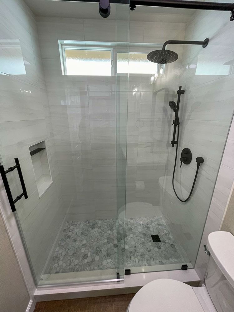 Modern bathroom with glass shower enclosure and black fixtures, featuring a pebble shower floor and white tiled walls.