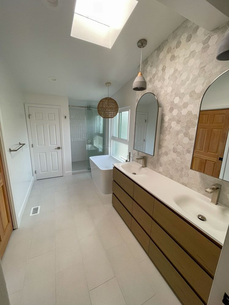 Modern bathroom with white and light wood elements. Features a long vanity with two sinks, a soaking tub, and a shower.
