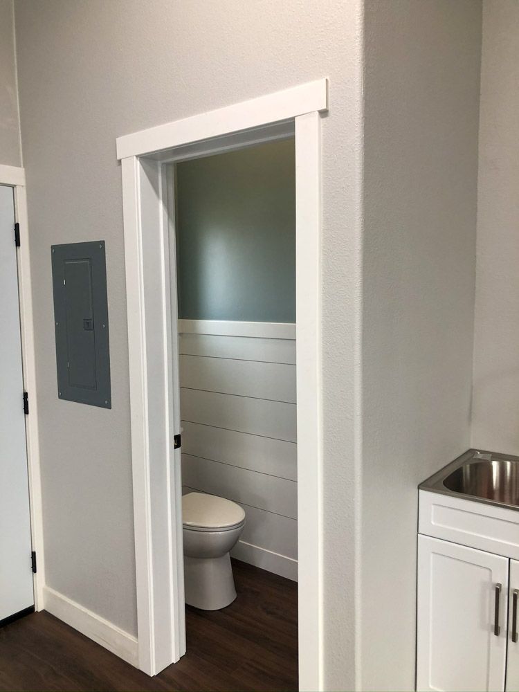 A small, interior bathroom with a toilet and wainscoting visible through the doorway. The walls are gray and white.