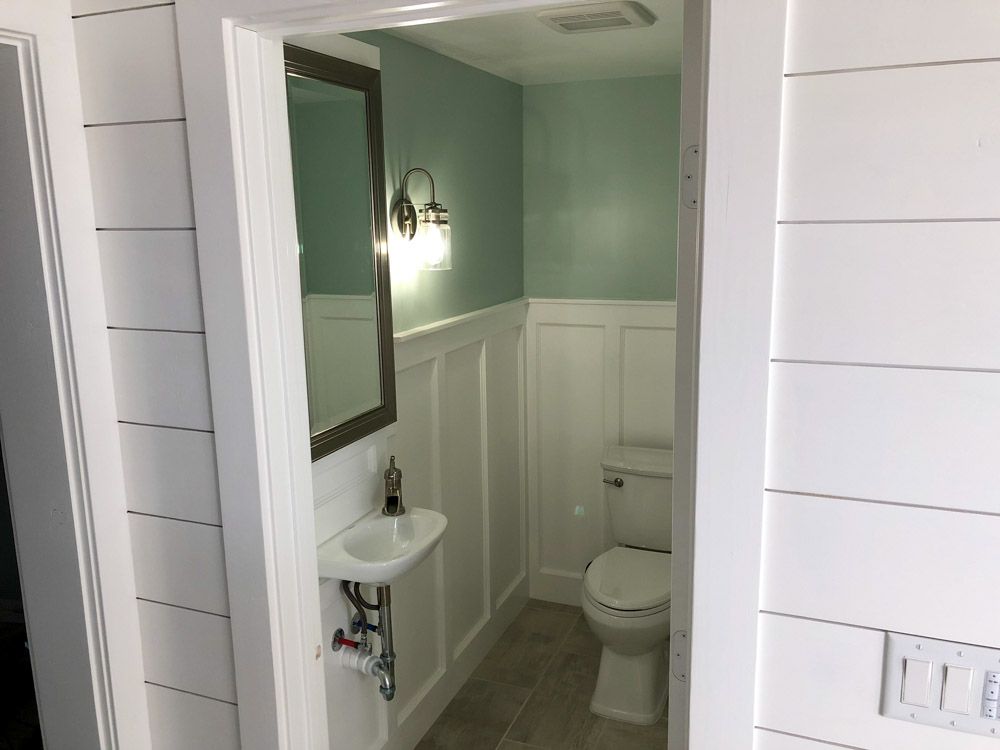 Small bathroom with white wainscoting and plank walls. A wall-mounted sink and toilet sit below a light blue wall.