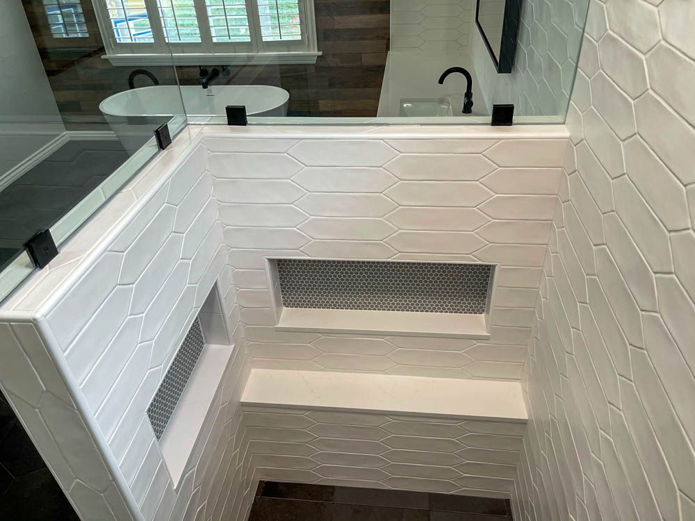Bathroom interior featuring a shower with white patterned tiles, a built-in bench, and a glass door. Black fixtures accent the space.