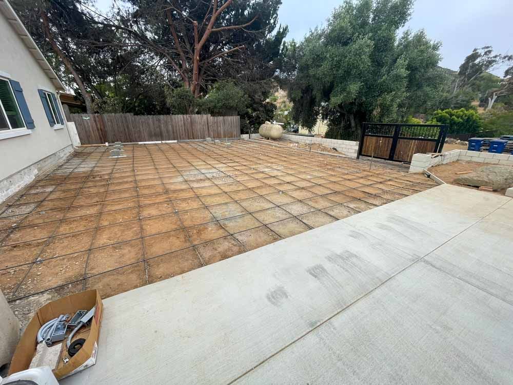 A construction site with a prepared area of rebar grid, likely for a concrete slab. A new driveway leads to it.