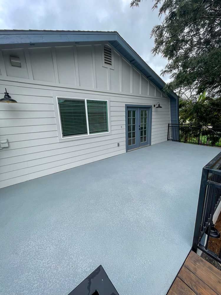Exterior view of a house with a gray deck. French doors, windows, and white siding are visible.