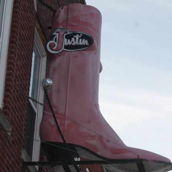 Large pink Justin boot sign mounted on a brick building, against a cloudy sky.