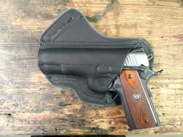 Black leather holster holding a silver and brown handgun on a wooden surface.