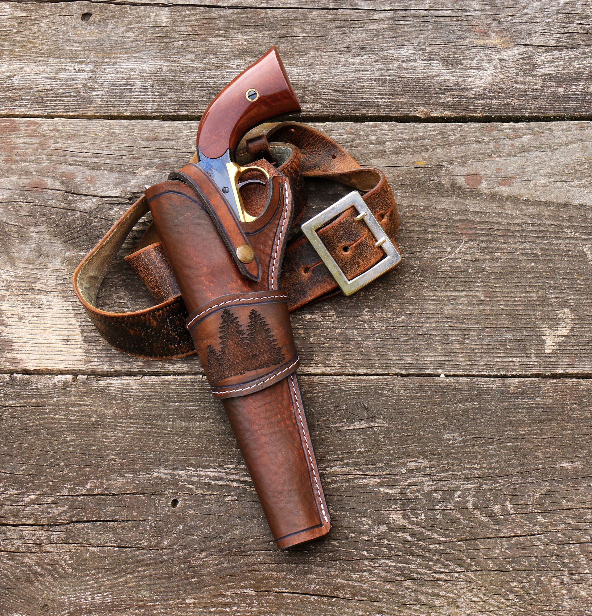 Leather holster with a revolver, on a wooden surface. Brown leather, dark wood grip, silver buckle.