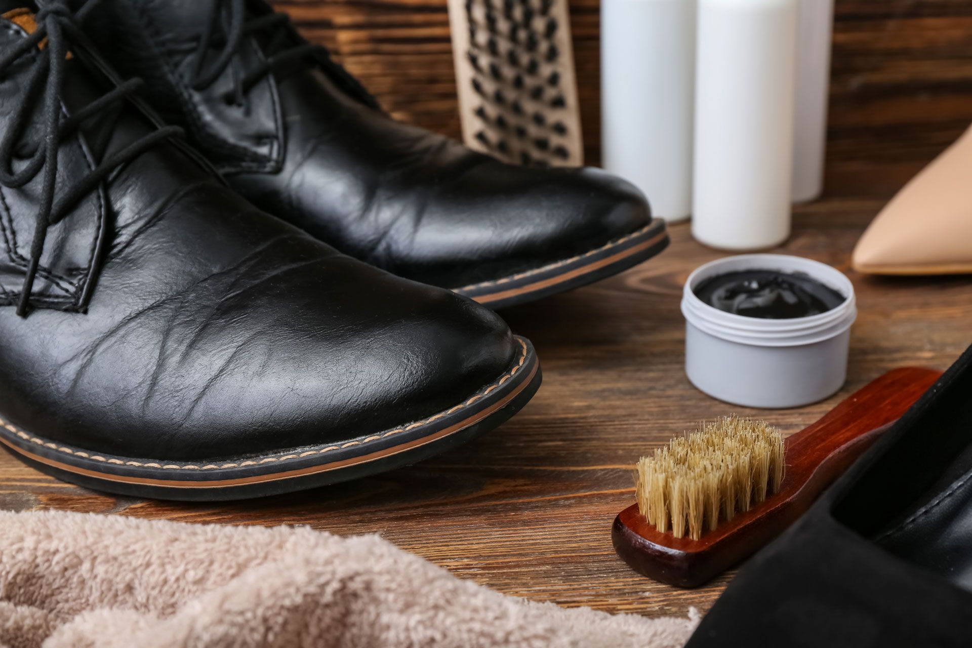 Black leather shoes being polished, with supplies on a wooden surface.
