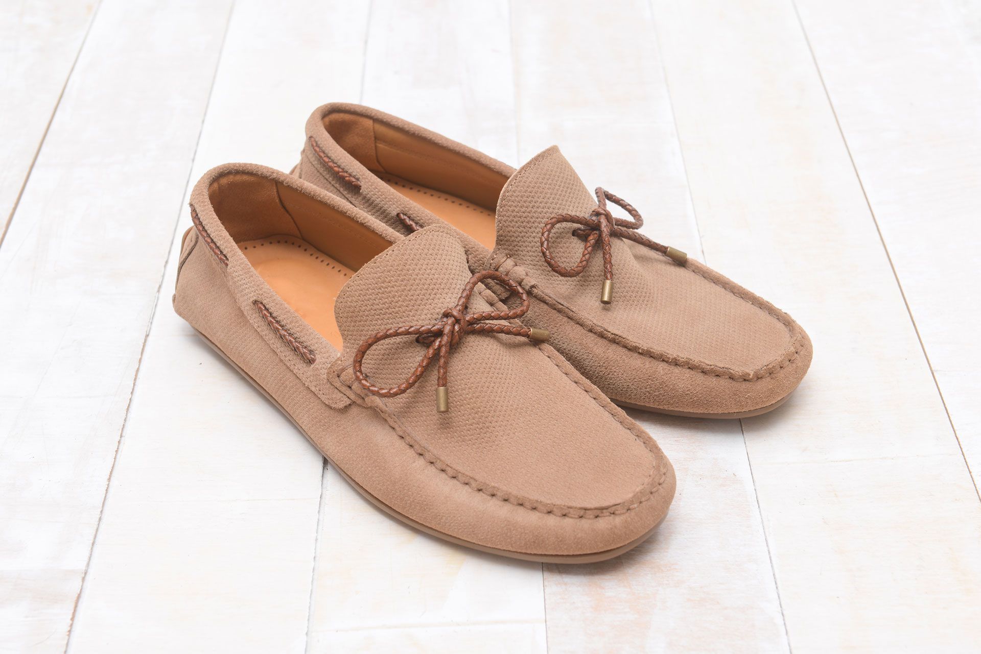 Beige suede loafers with brown laces on white wood.