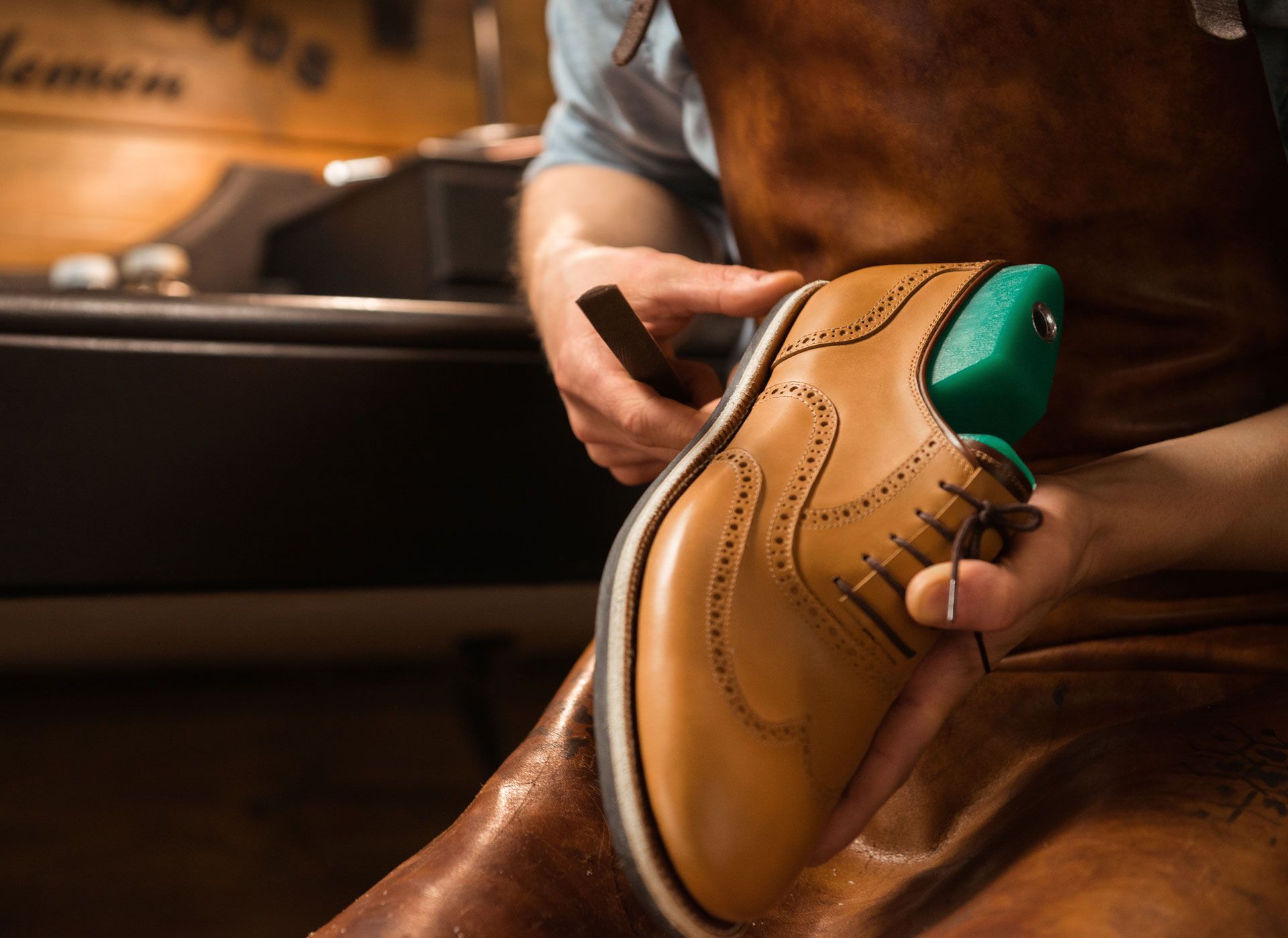 Shoemaker working on a tan leather shoe with a green shoe last.
