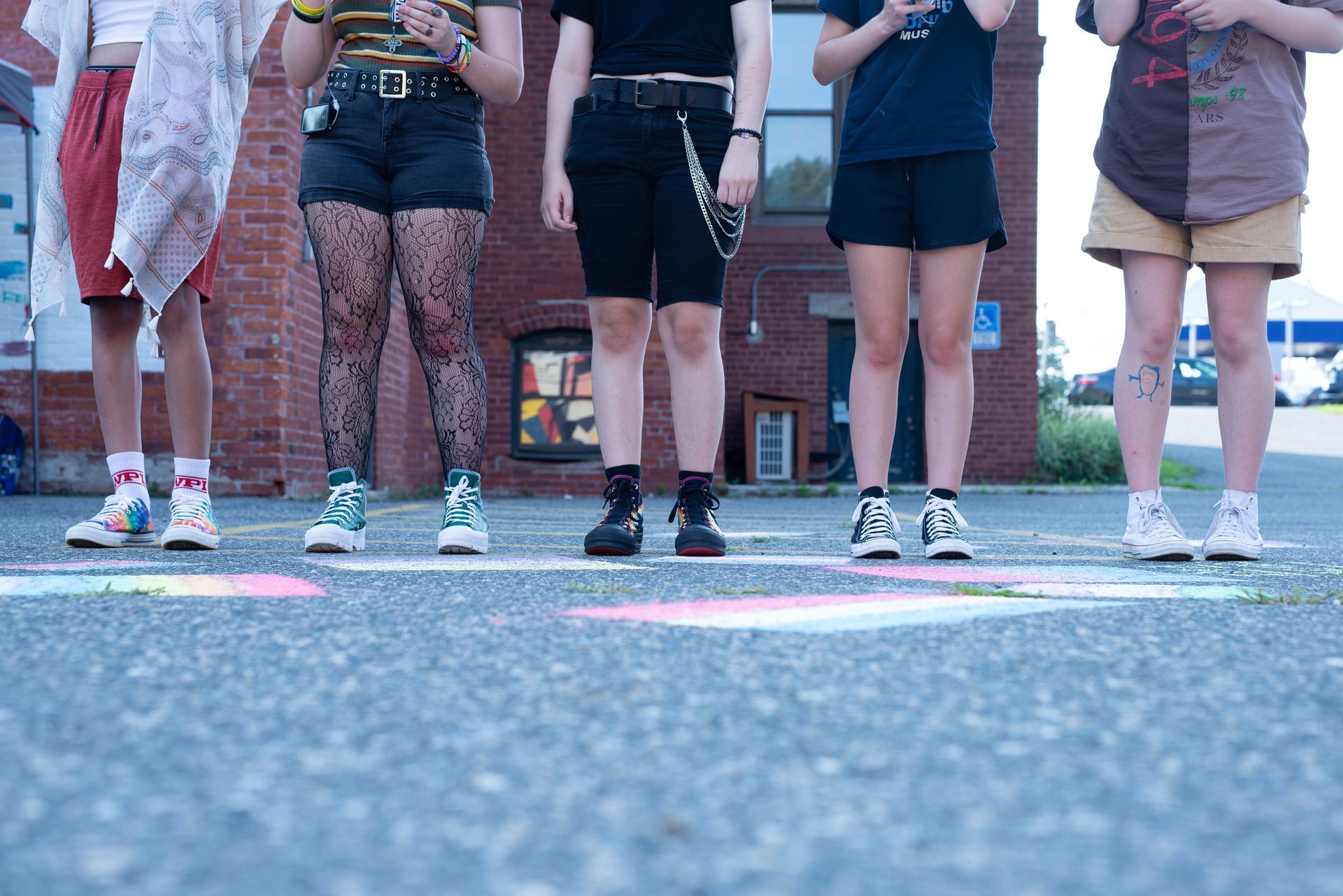 Five people standing on a street, legs and feet visible. Each stands on a chalk square.