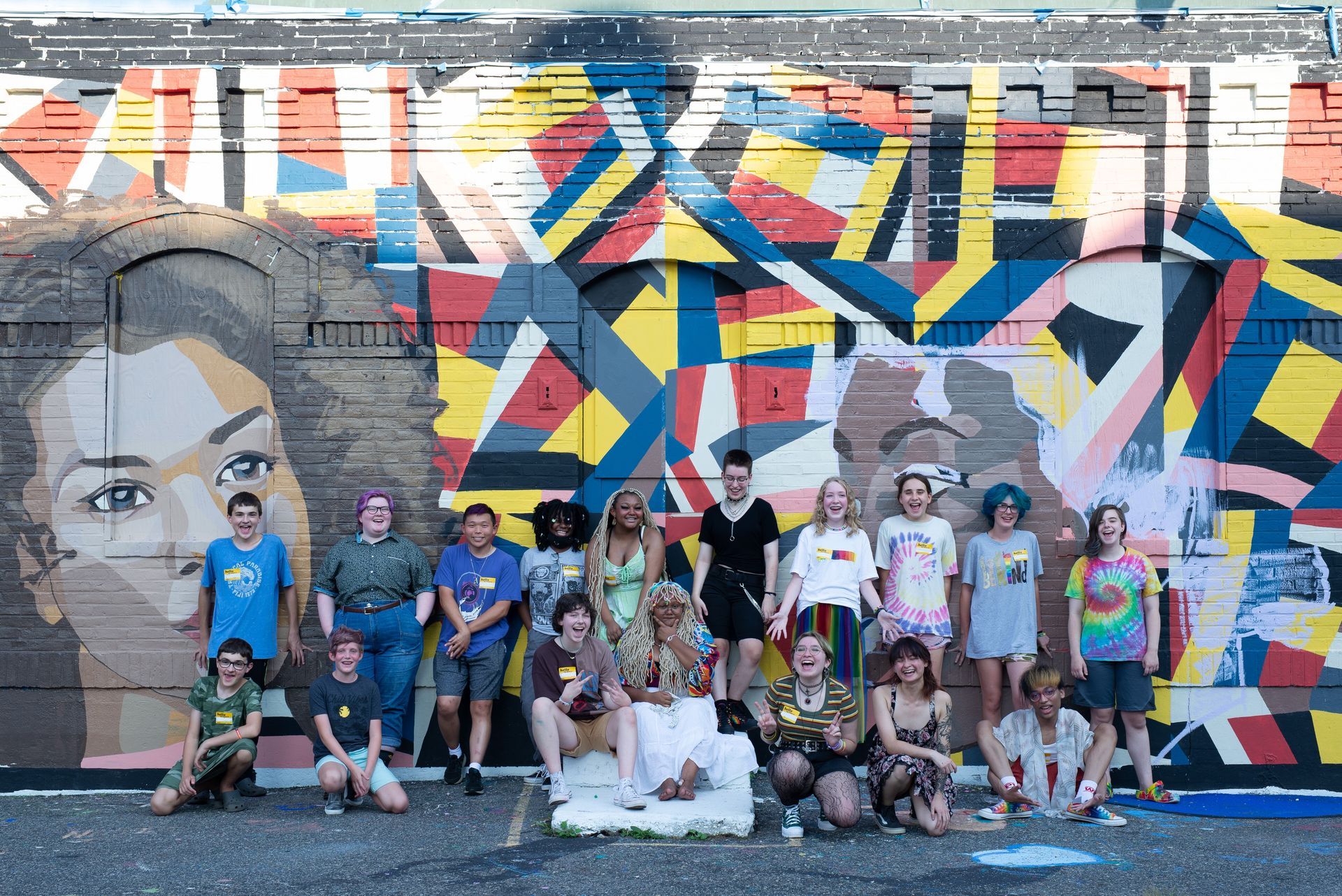 Group of people pose in front of a colorful mural outdoors.