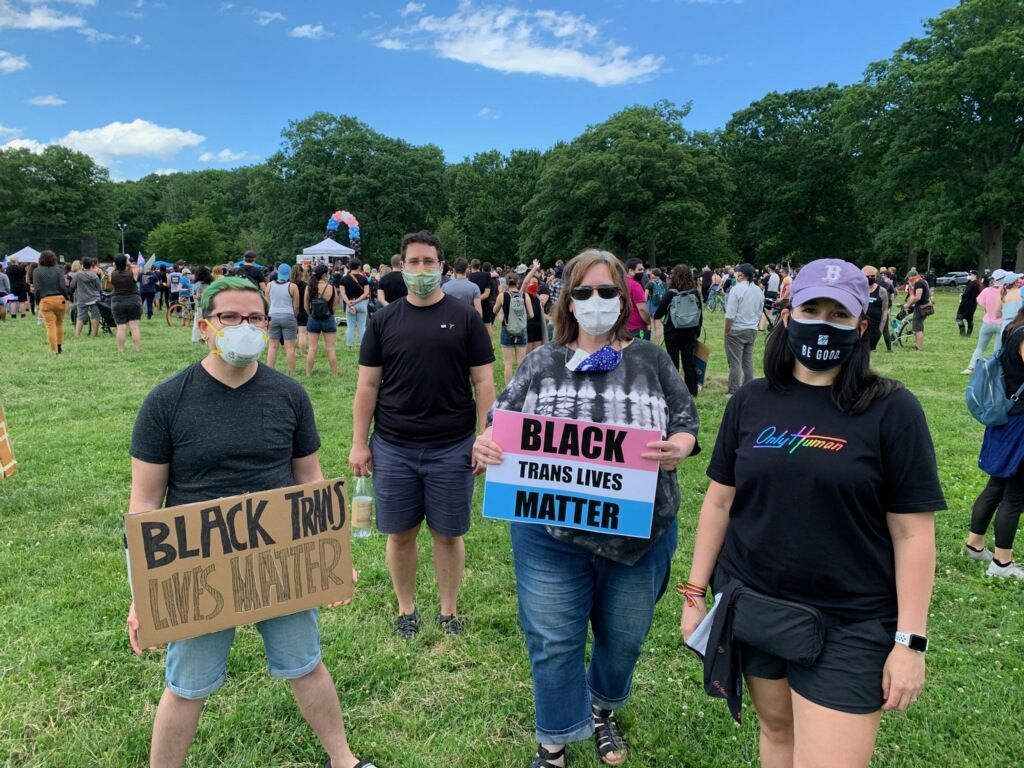 People holding signs at an outdoor gathering. Signs read
