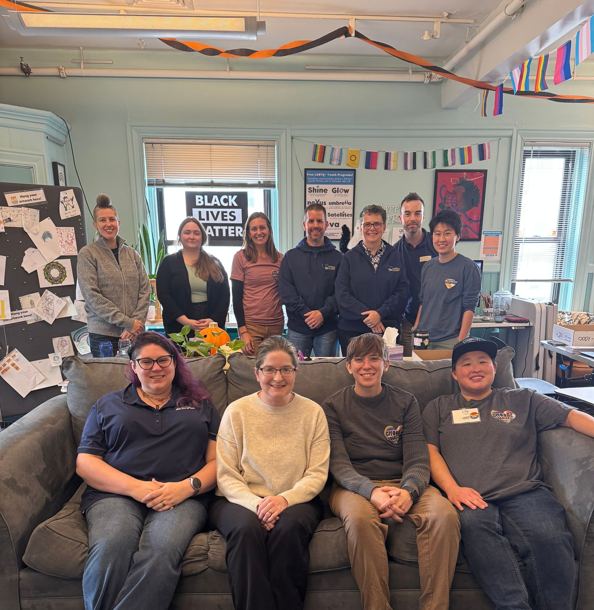 Group of people posing for a photo indoors, some seated on a couch, with decorations and a