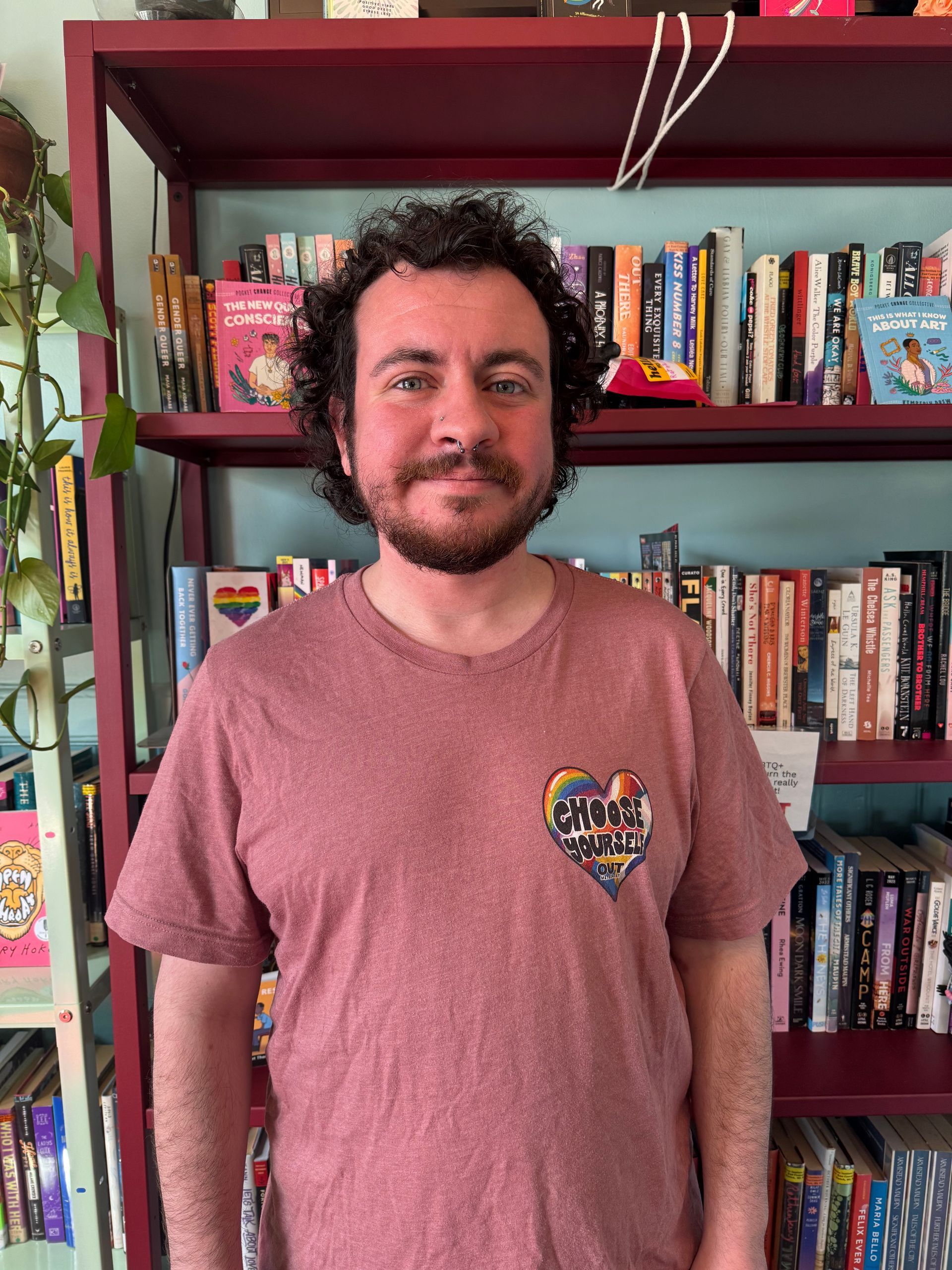 Person with glasses and a cap, smiling at a baseball game, with a crowd and red seats in the background.