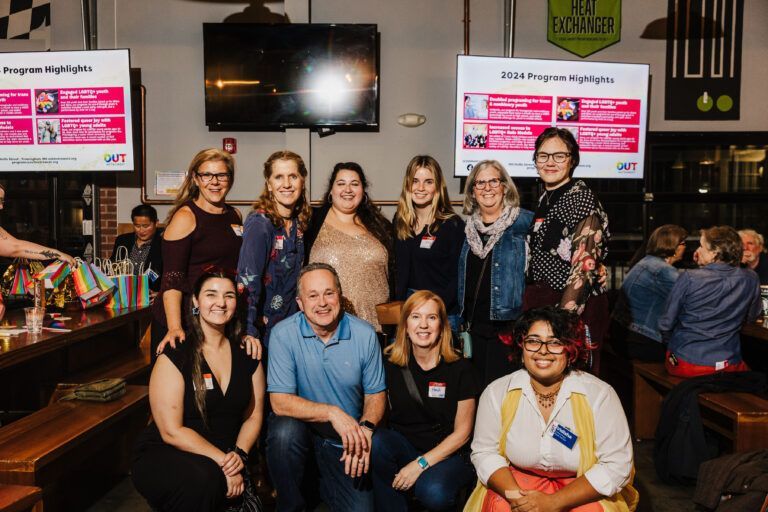 Group of people posing for a photo in a casual setting with two projection screens.