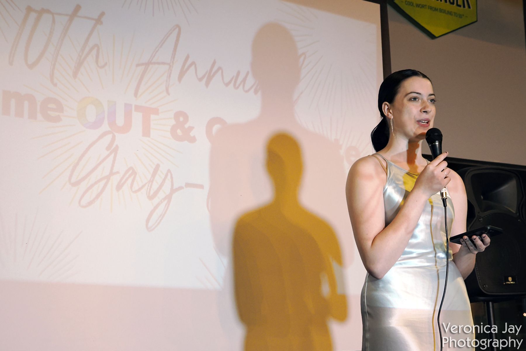 Woman speaking into a microphone at an event, shadow on a screen, words 
