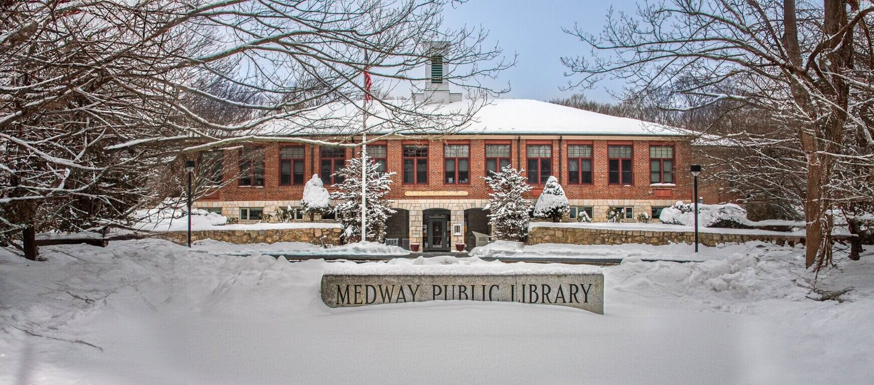 Medway Public Library in winter, snow-covered building with sign and bare trees.