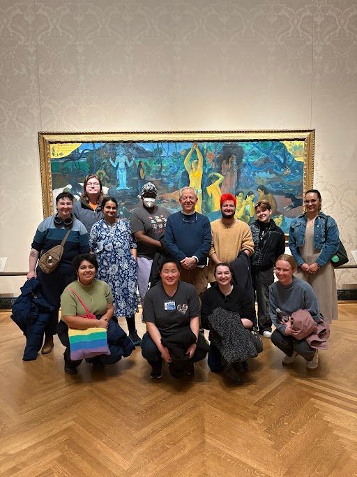 Group of people pose in front of a colorful painting at a museum.