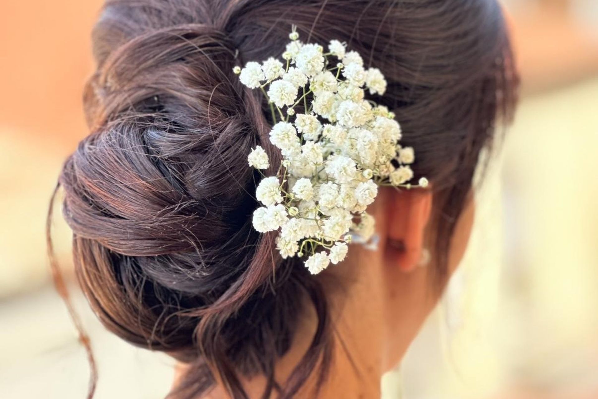 Donna con i capelli scuri raccolti in uno chignon, adornata con un mazzo di fiori bianchi di gypsophila.
