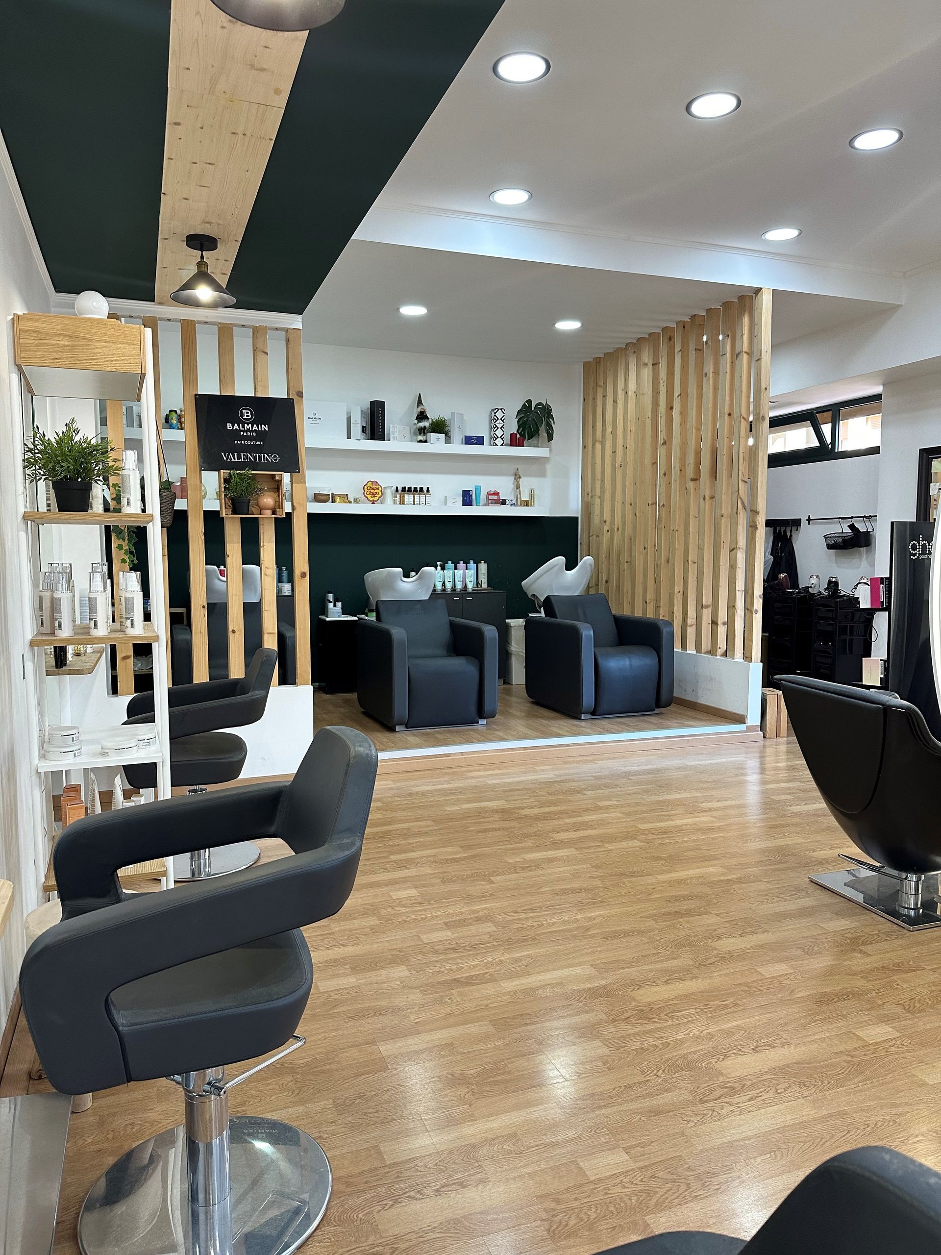 Interno di un salone da parrucchiere con sedie, lavandini, scaffali e divisori in legno.