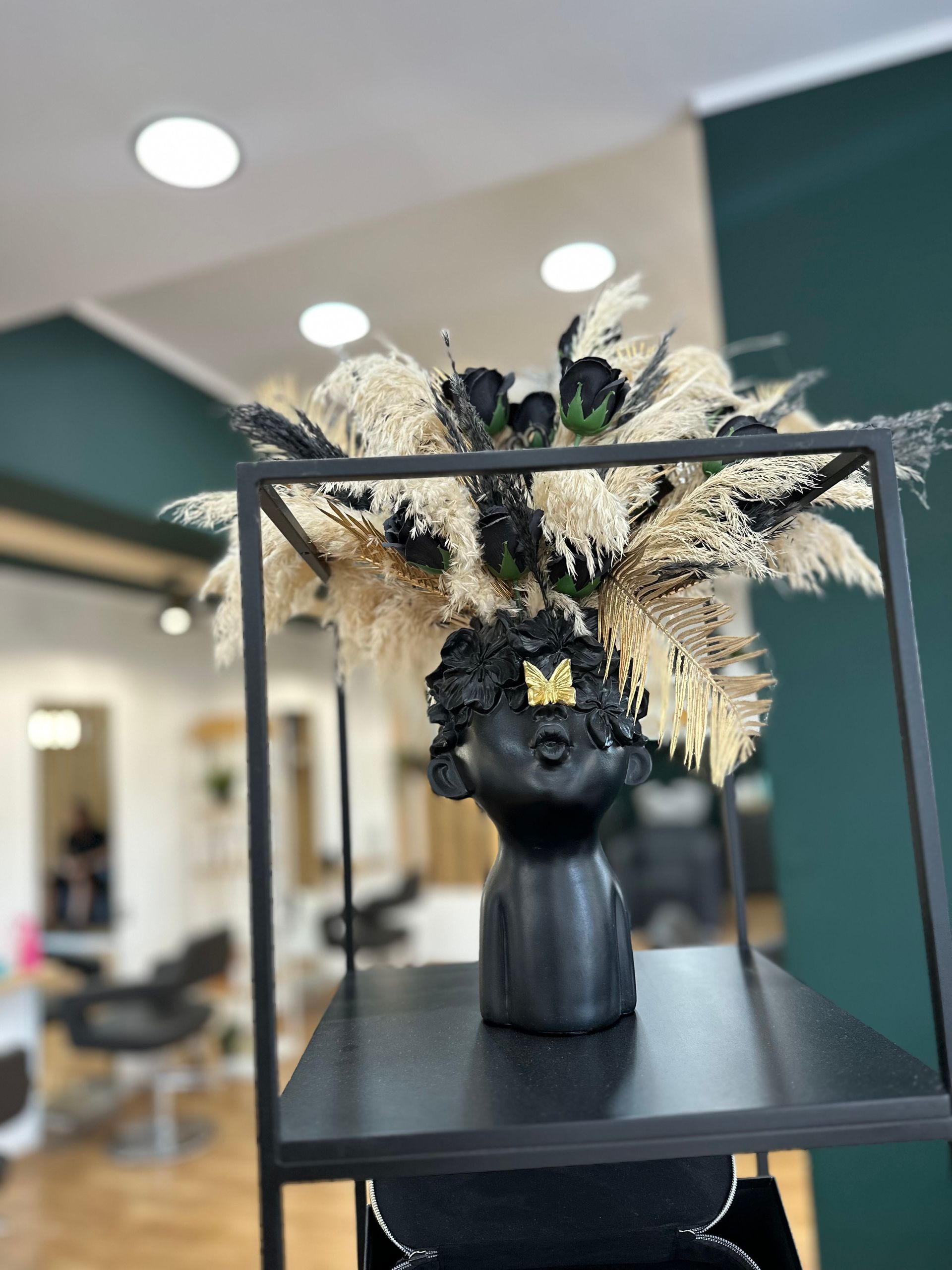 Vaso nero a forma di testa, con erba della pampa e fiori neri; situato in un salone.