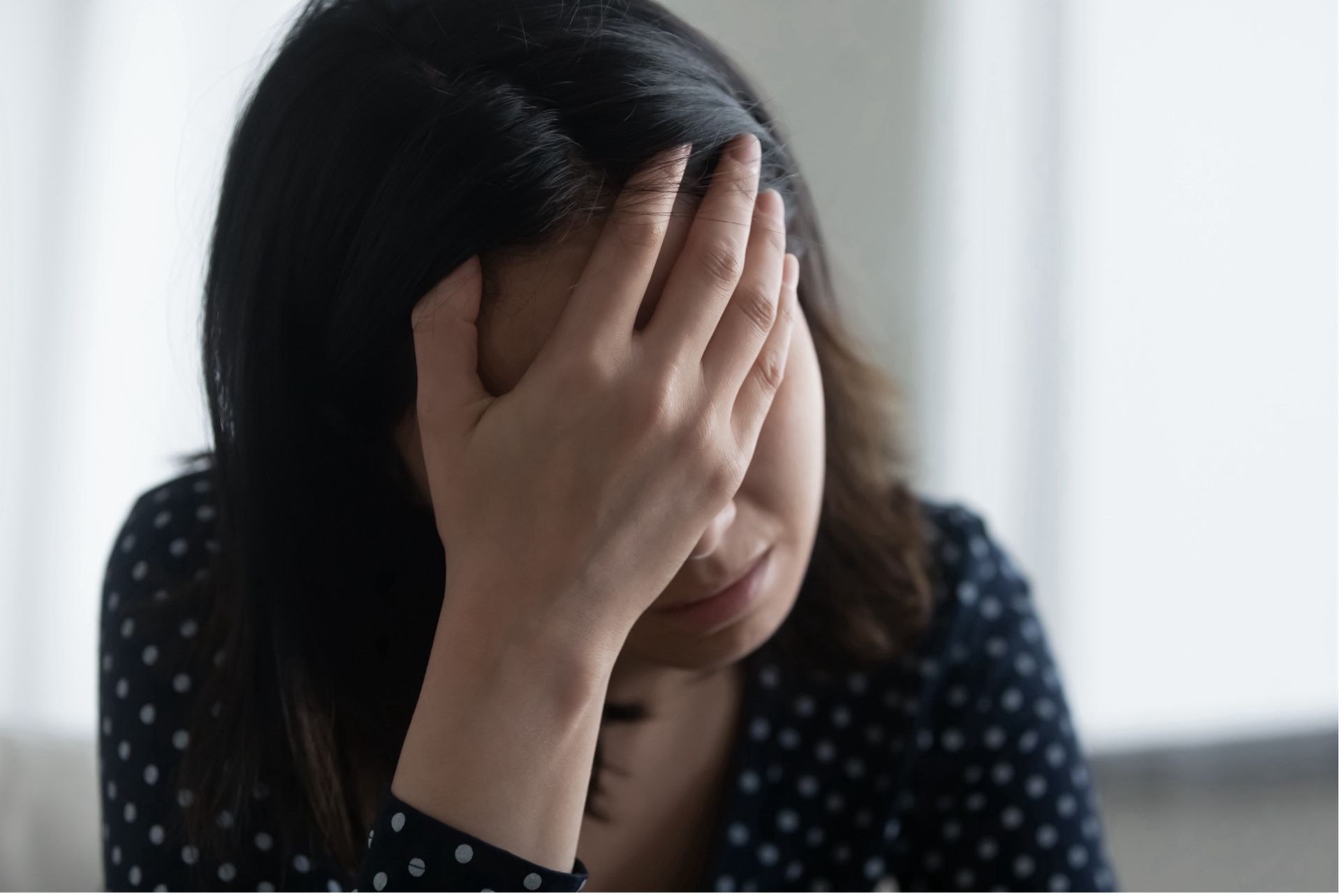 Woman with dark hair, hand covering face, showing a look of distress.