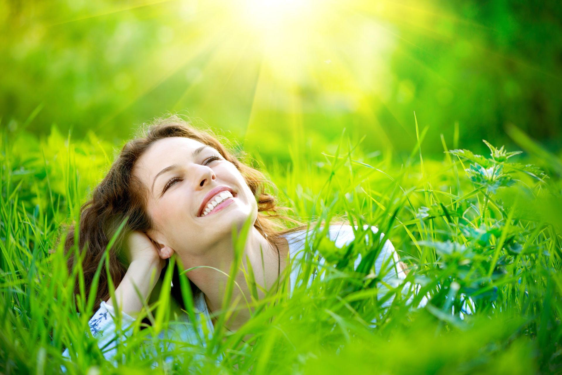 Woman smiling and lying in green grass, bathed in sunlight.