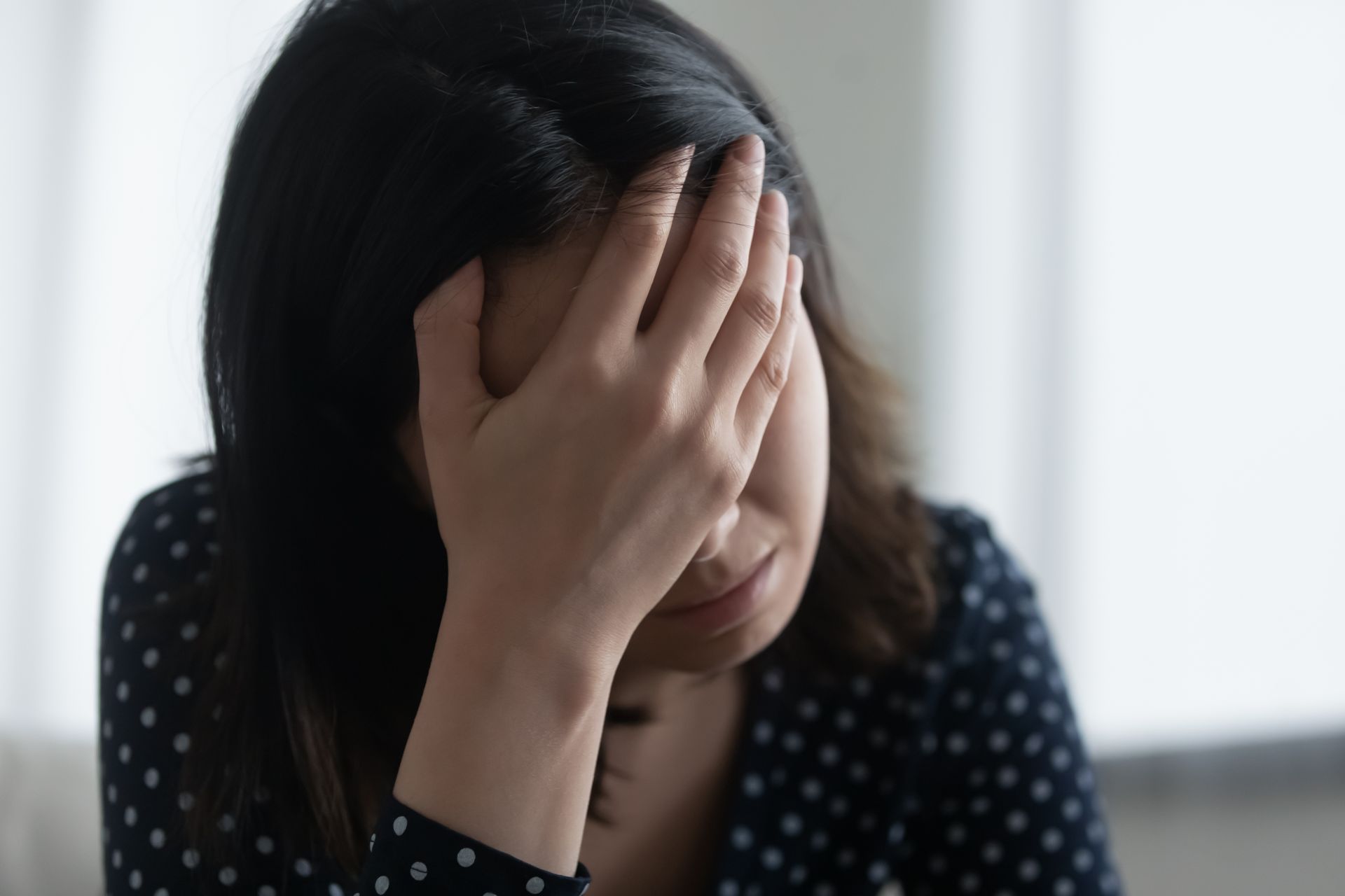 Woman with dark hair covers her face with her hand, displaying a look of sadness or stress.