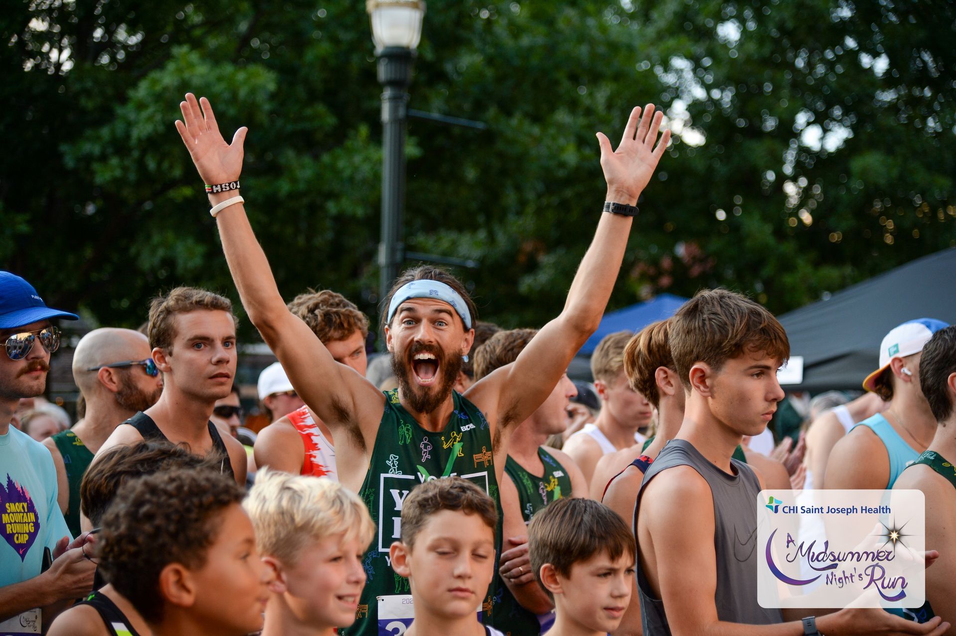 Man with arms raised celebrating victory at a race, surrounded by a crowd of runners.