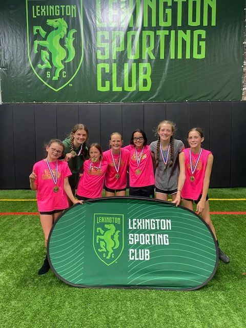 Basketball player dunking, leaping toward the hoop, with a defender attempting to block. Spectators in the background.