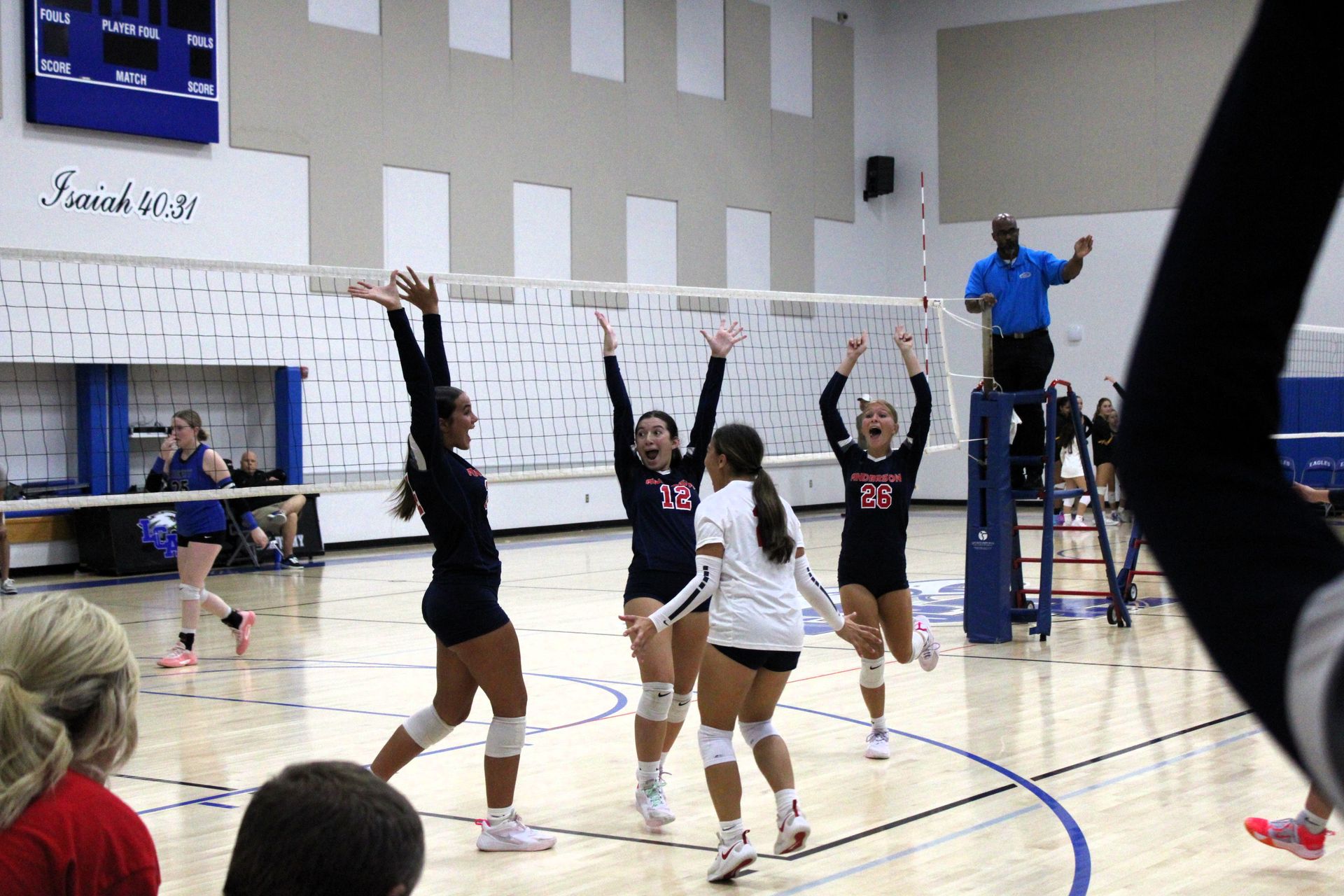 Volleyball players celebrate a point near the net. Players wear black and white uniforms in a gym.