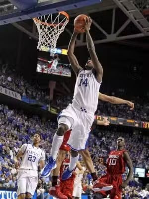 Basketball player in white jersey, number 14, jumping to shoot the ball near the hoop, another player attempting to block.