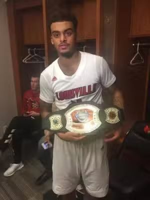 Basketball player holding championship belt, wearing white jersey with
