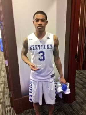 Basketball player in Kentucky jersey holding an award and shoes.