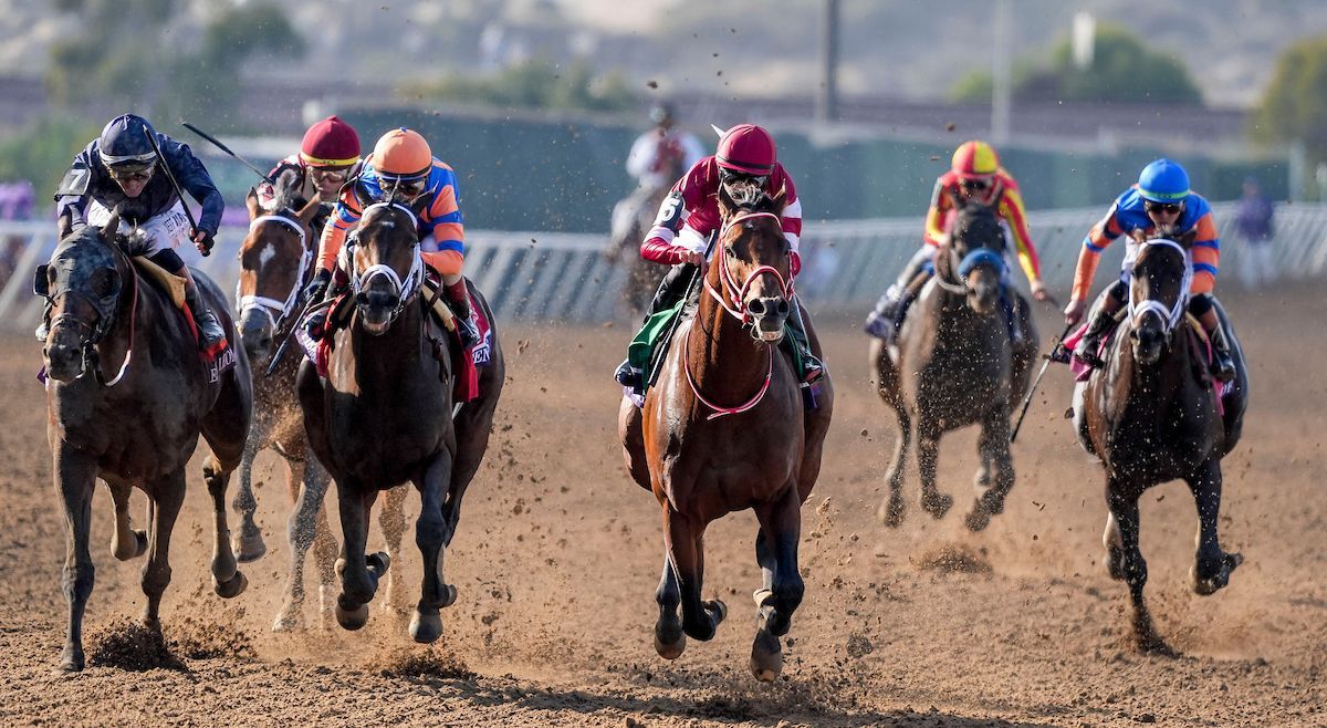 Horses racing on a dirt track, jockeys in colorful silks.