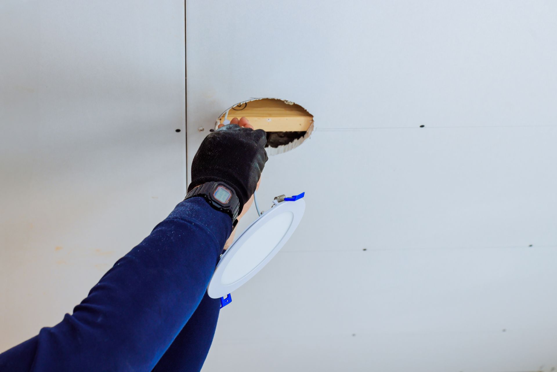 A person in gloves installs a round recessed LED light into a hole in a white ceiling.