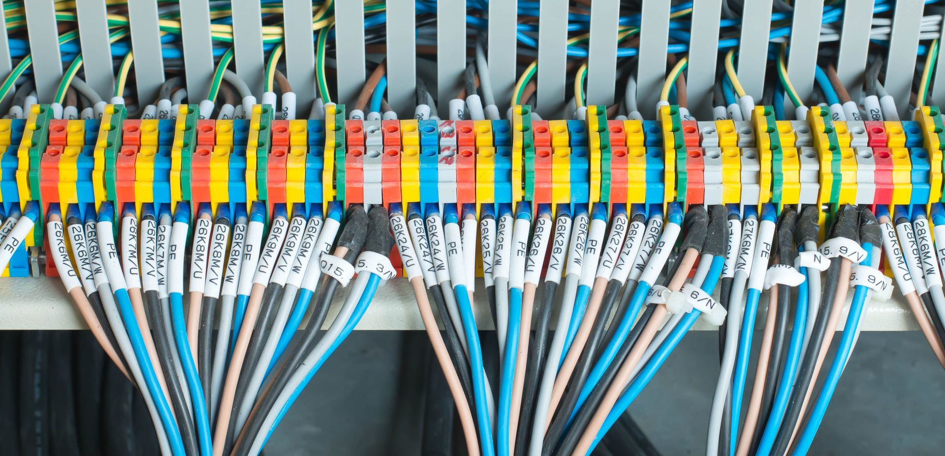 A row of colorful electrical terminal blocks wired with numerous labeled cables inside a control panel.
