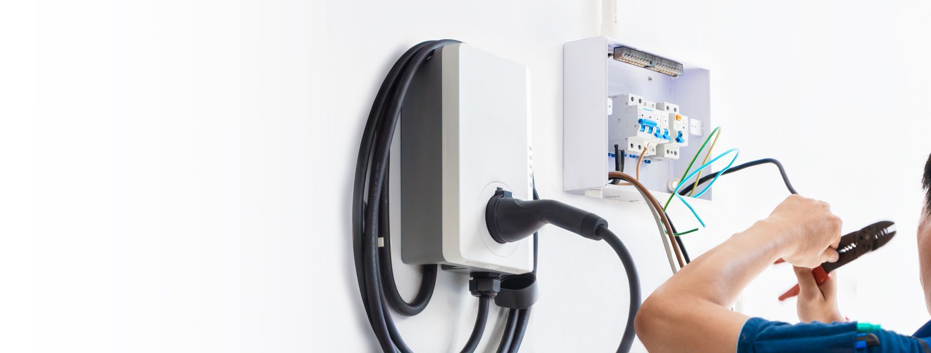 An electrician installs an electric vehicle charging station on a white wall.