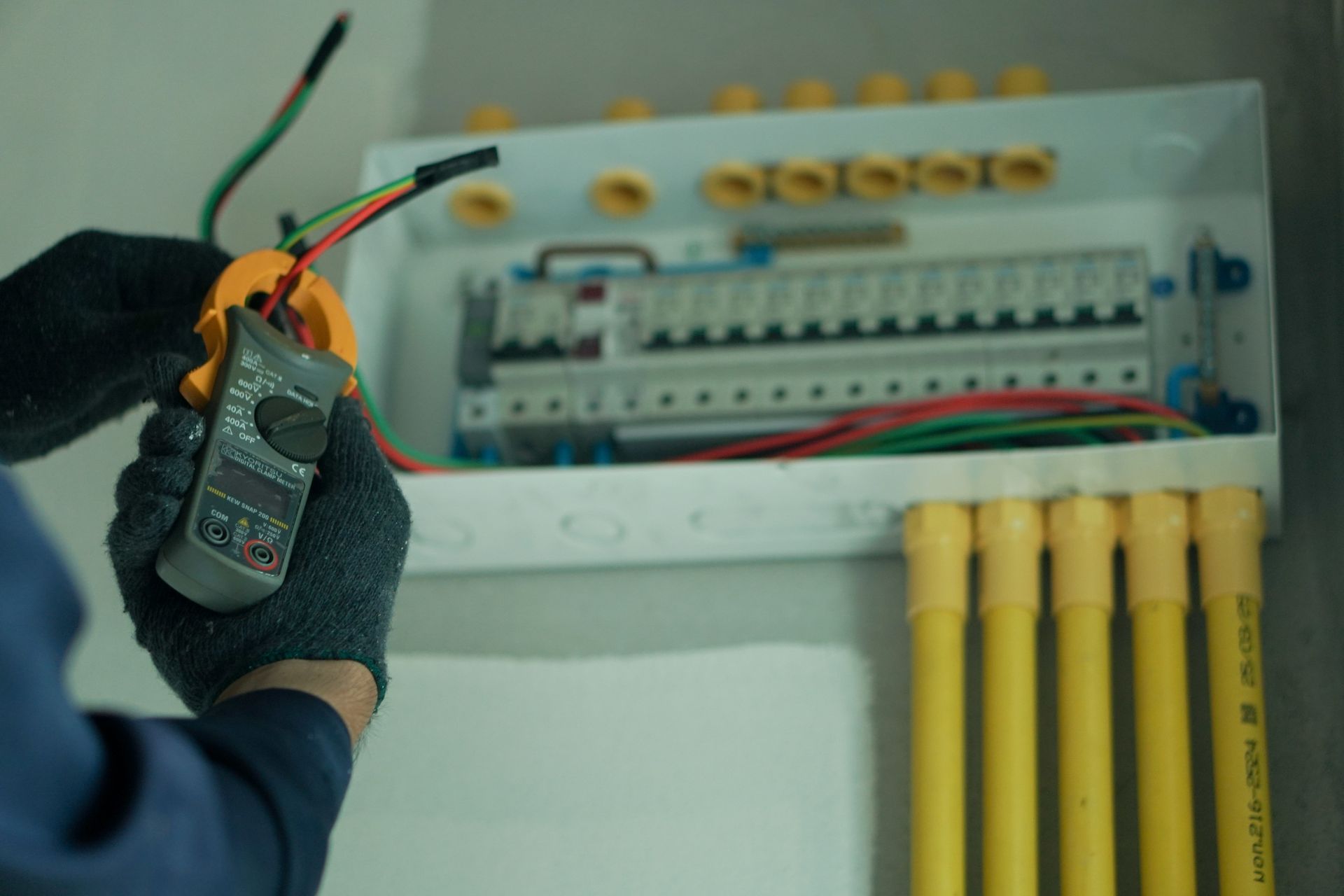 An electrician uses a clamp meter to measure current on electrical wires connected to a breaker box.