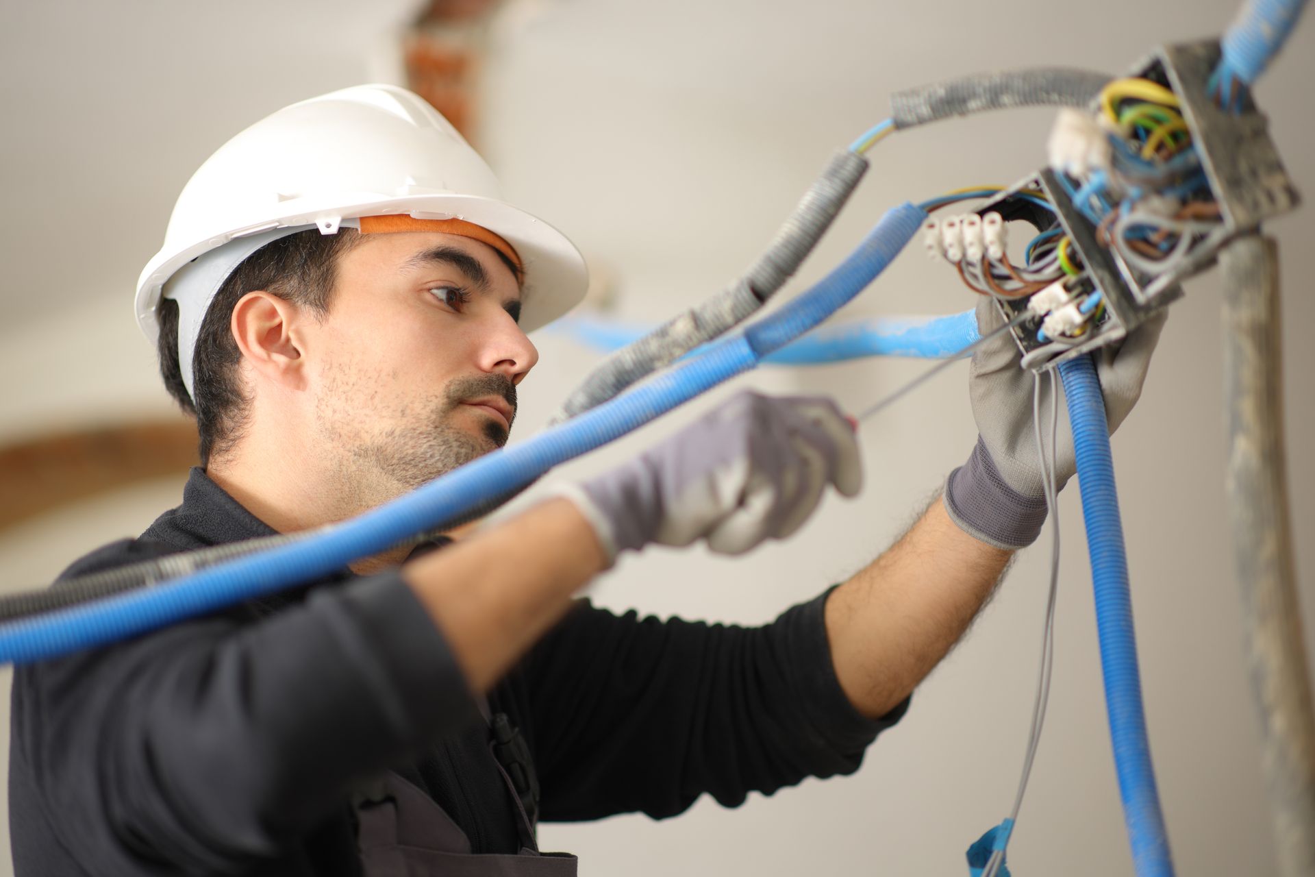 Electrician in a hard hat working on blue cables and a junction box indoors.
