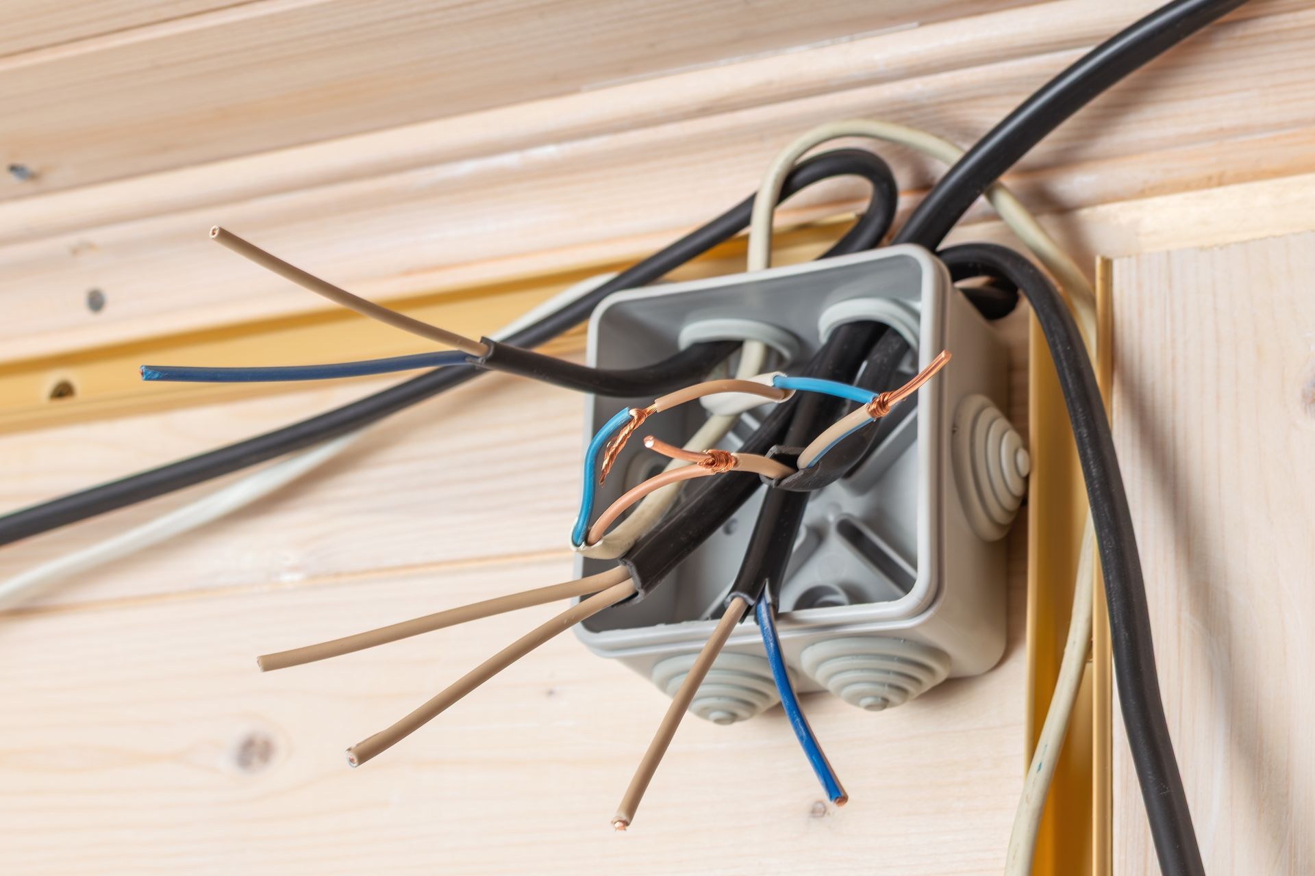 An open junction box mounted on a wooden wall, containing exposed, unfinished electrical wiring.